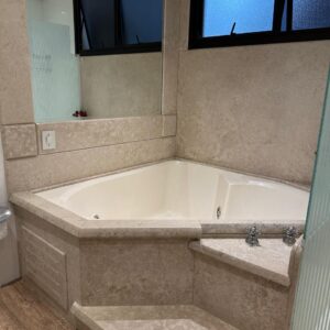 BANHEIRA TRIANGULAR JACUZZI — OFF WHITE — BANCADA E PAREDES LATERAIS REVESTIDAS DE TRAVERTINO — MOTOR