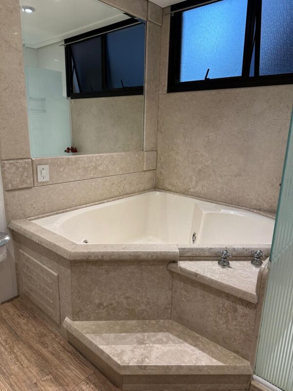 BANHEIRA TRIANGULAR JACUZZI — OFF WHITE — BANCADA E PAREDES LATERAIS REVESTIDAS DE TRAVERTINO — MOTOR