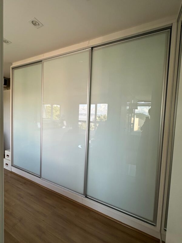 ARMÁRIO EM “L” — PORTAS DE CORRER — 3 DELAS DE VIDRO SERIGRAFADO + 2 DELAS EM ESPELHO — PARTE INTERNA COMPOSTA POR GAVETAS, PRATELEIRAS, ARARAS, GAVETAS COM DIVISÓRIAS PARA BIJUS, CALCEIROS, ÁREA PARA ROUPAS LONGAS — MDF COM LACA BRANCA — NICHOS LATERAIS COM ILUMINAÇÃO - Imagem 5
